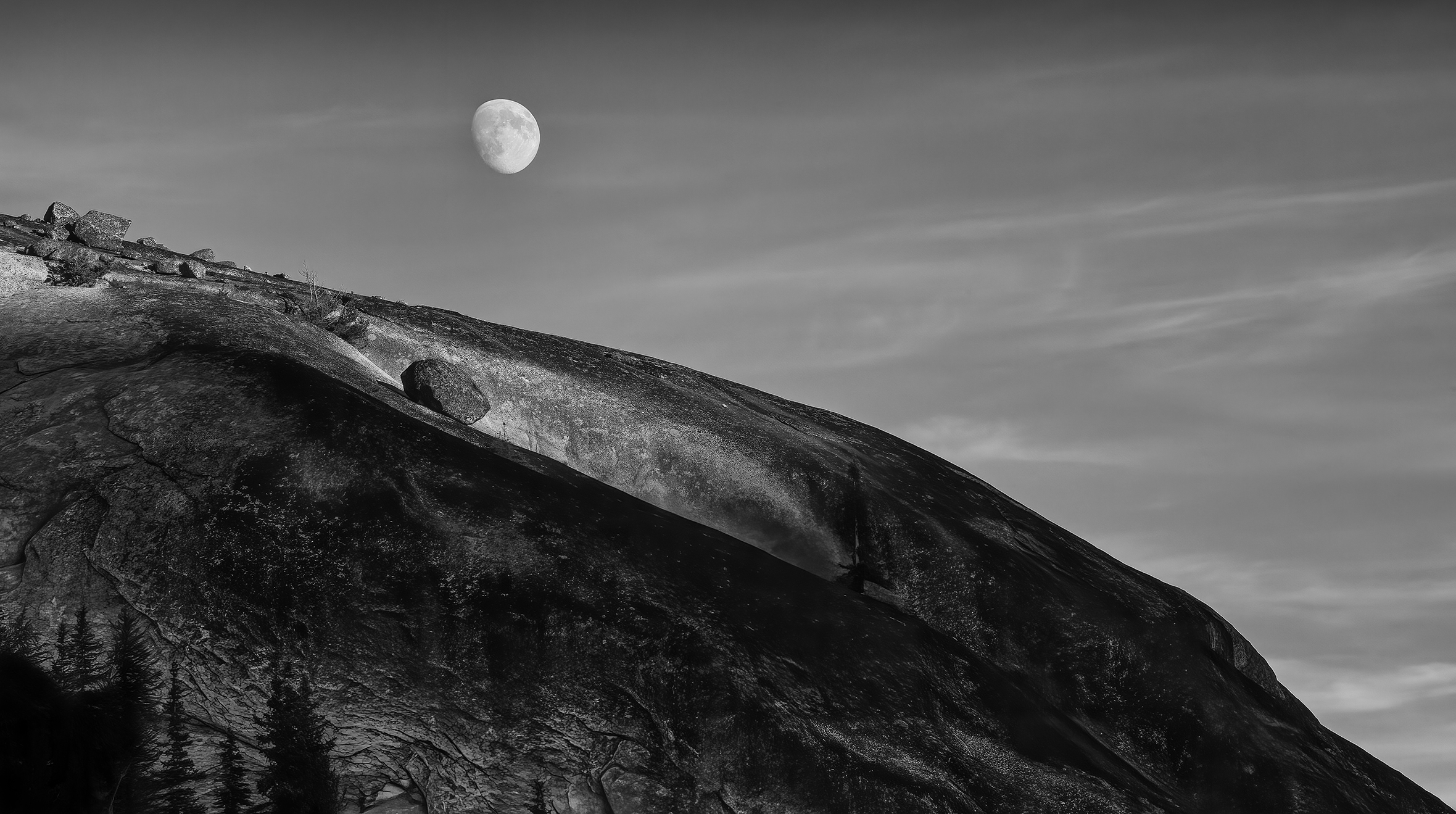 Moon above a bare and rocky mountaintop.